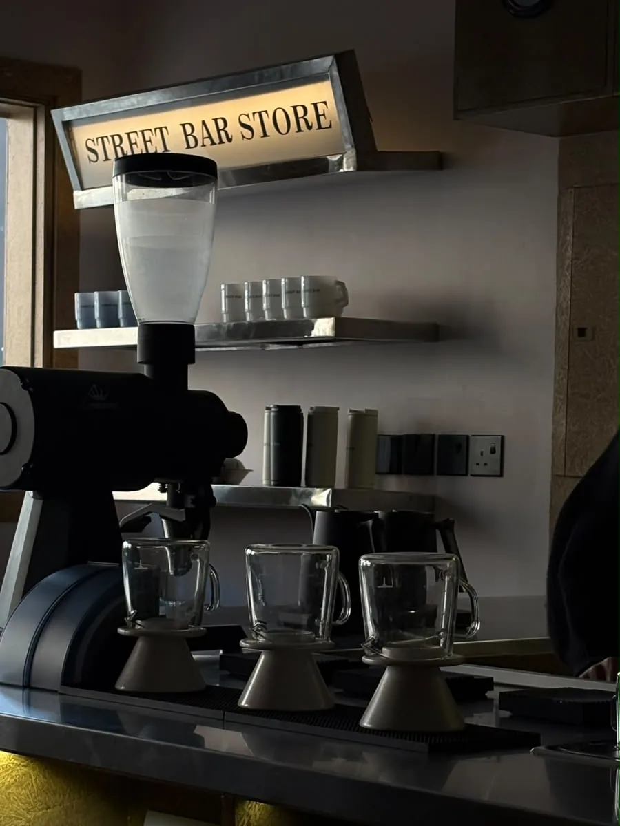 مطحنة القهوة وأكواب زجاجية على البار، وفوقها لوحة STREET BAR STORE المضيئة